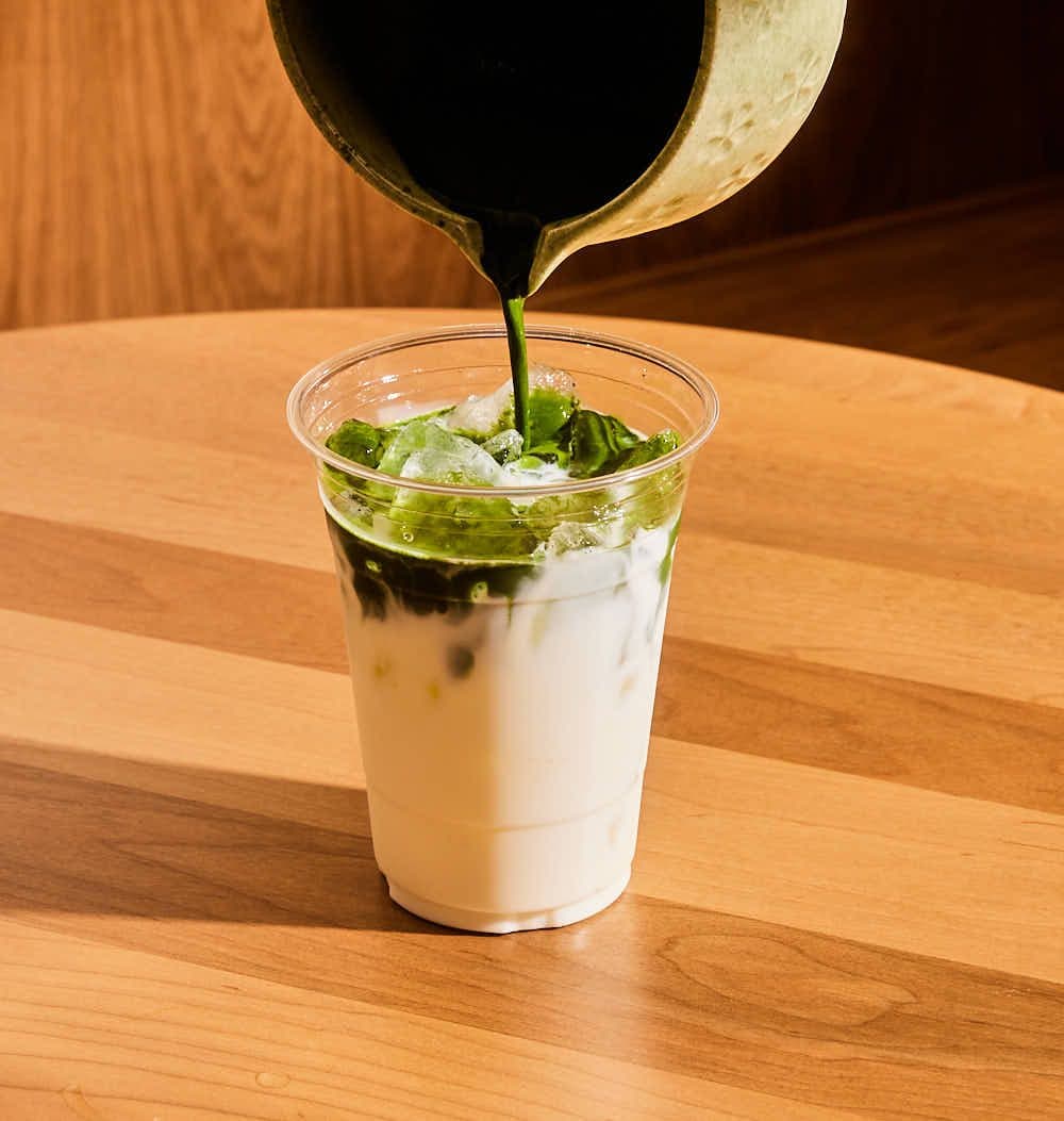 Matcha being poured over an iced milk latte